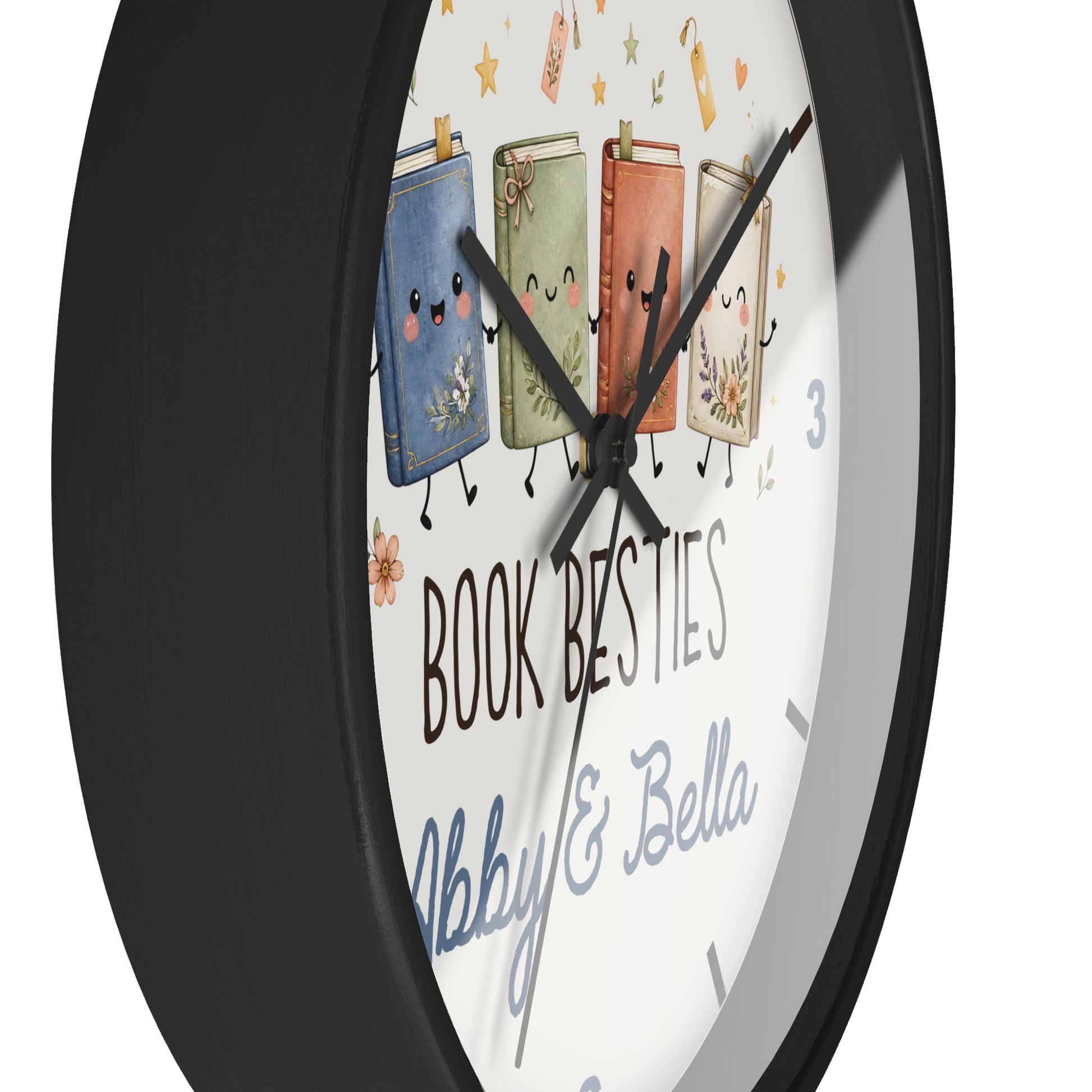A round wall clock with a black frame and a white face featuring four smiling illustrated books and the text 'BOOK BESTIES Abby & Bella'.