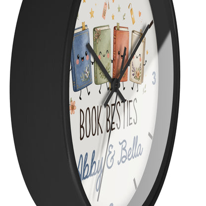 A round wall clock with a black frame and a white face featuring four smiling illustrated books and the text 'BOOK BESTIES Abby & Bella'.