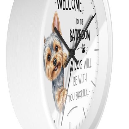 A round white wall clock with a printed illustration of a Yorkshire Terrier and the text 'WELCOME TO THE BATHROOM A DOG WILL BE WITH YOU SHORTLY' on the face.
