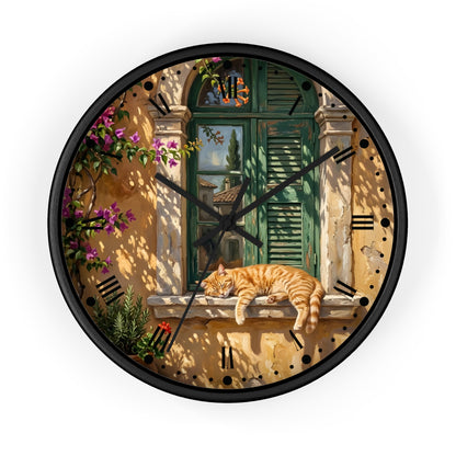 A round wall clock with a black frame and hands, featuring a printed scenic design of a warm stone wall, green shutters, climbing flowers, and an orange tabby cat resting on a windowsill. Roman numerals mark the hours.