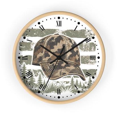 Round wall clock with a light wood frame, featuring a camouflage baseball cap graphic over a distressed olive green and white American flag design, with black Roman numerals and clock hands on a white face.