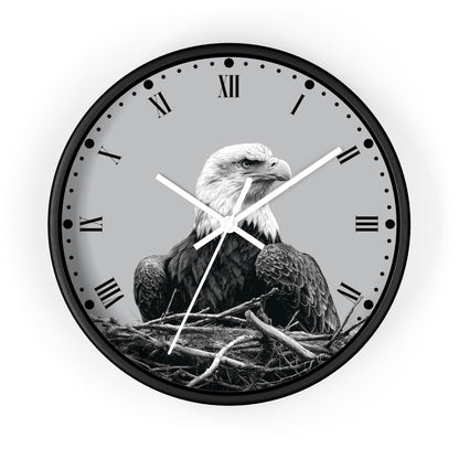 Round wall clock with a black frame and a grayscale bald eagle perched in a nest on the clock face, with Roman numerals and white hands, shown against a light gray background.