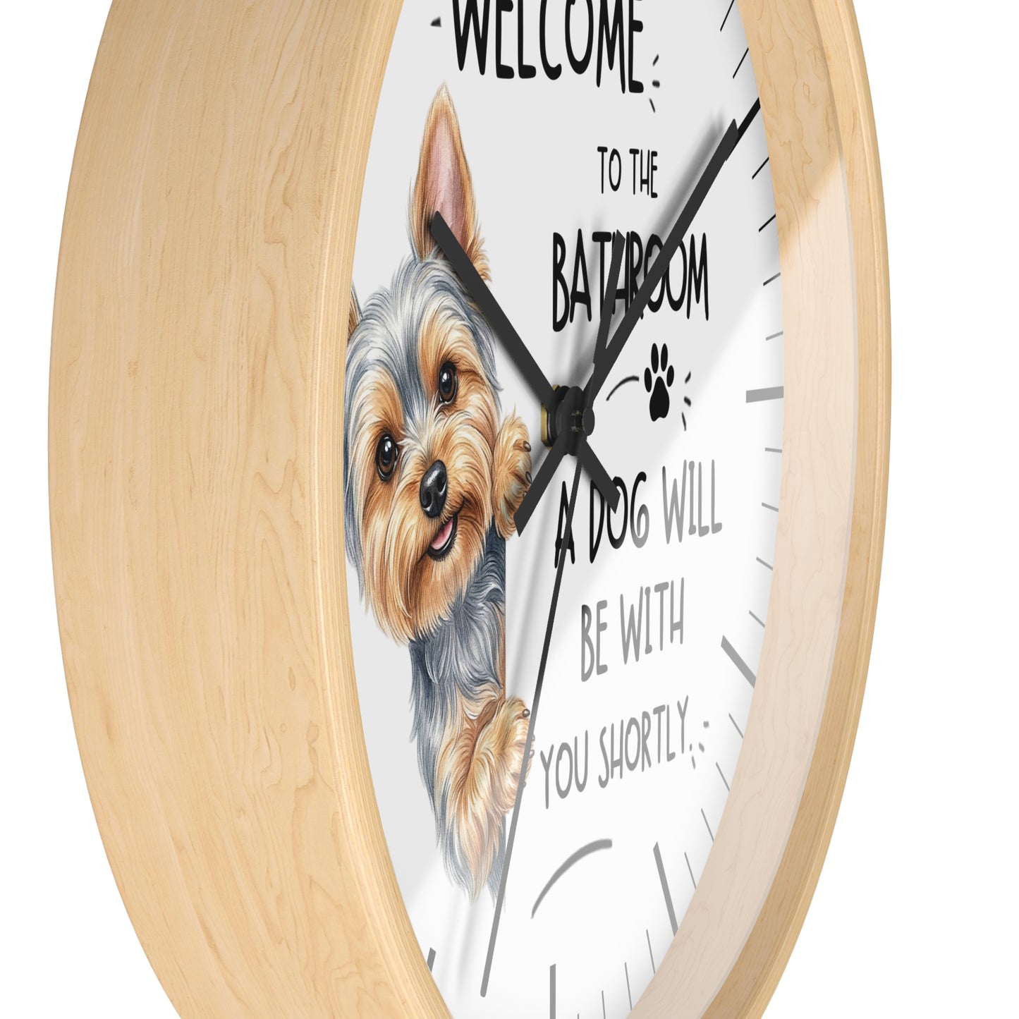 A round wall clock with a light natural wood frame and a white face. The clock features a hand-drawn illustration of a Yorkshire Terrier dog and the humorous text 'WELCOME TO THE BATROOM A DOG WILL BE WITH YOU SHORTLY'.