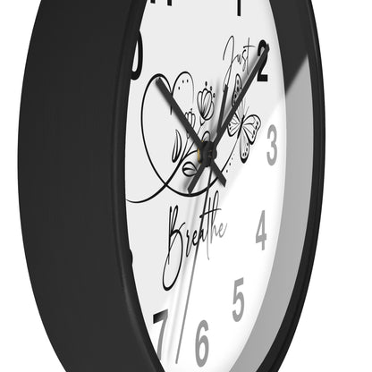 A close-up of a round wall clock with a black frame and a white face featuring black numerals, script text reading 'Just Breathe,' and butterfly and heart illustrations.