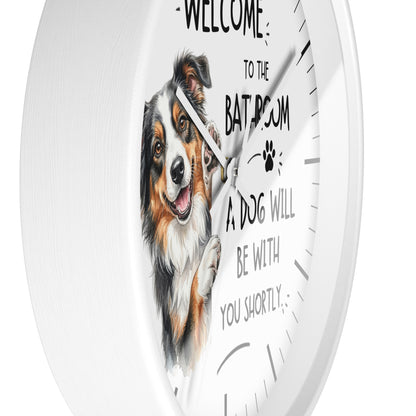A white round wall clock with a printed illustration of a smiling dog and the text 'WELCOME TO THE BATHROOM A DOG WILL BE WITH YOU SHORTLY' on the front.