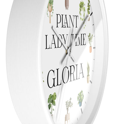 A white round wall clock with a minimalist design, featuring the text 'PLANT LADY TIME GLORIA' in black serif font and delicate illustrations of potted green plants around the dial.