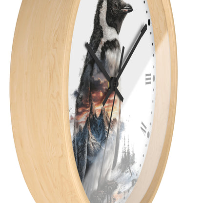 Round wall clock with a light natural wood frame and a printed face showing a penguin standing in snowy mountains under a dramatic orange sky.