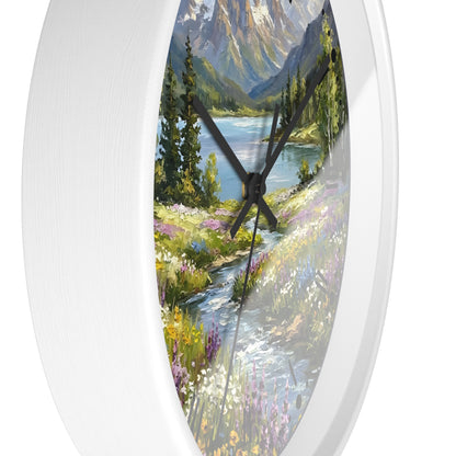 An oval wall clock with a white frame and a scenic landscape print featuring a mountain lake, trees, and a wildflower meadow, shown against a plain white background.