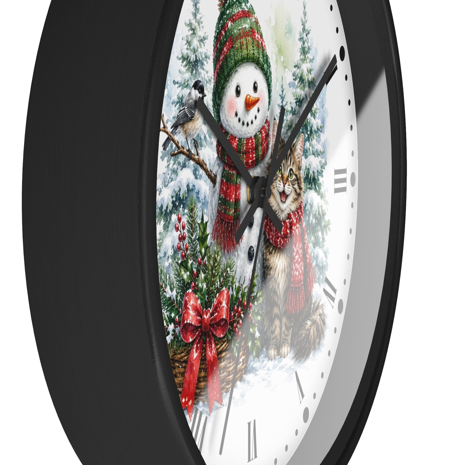 A round wall clock with a black frame and a white face featuring a festive winter illustration of a snowman, a cat, evergreen trees, and red bows.