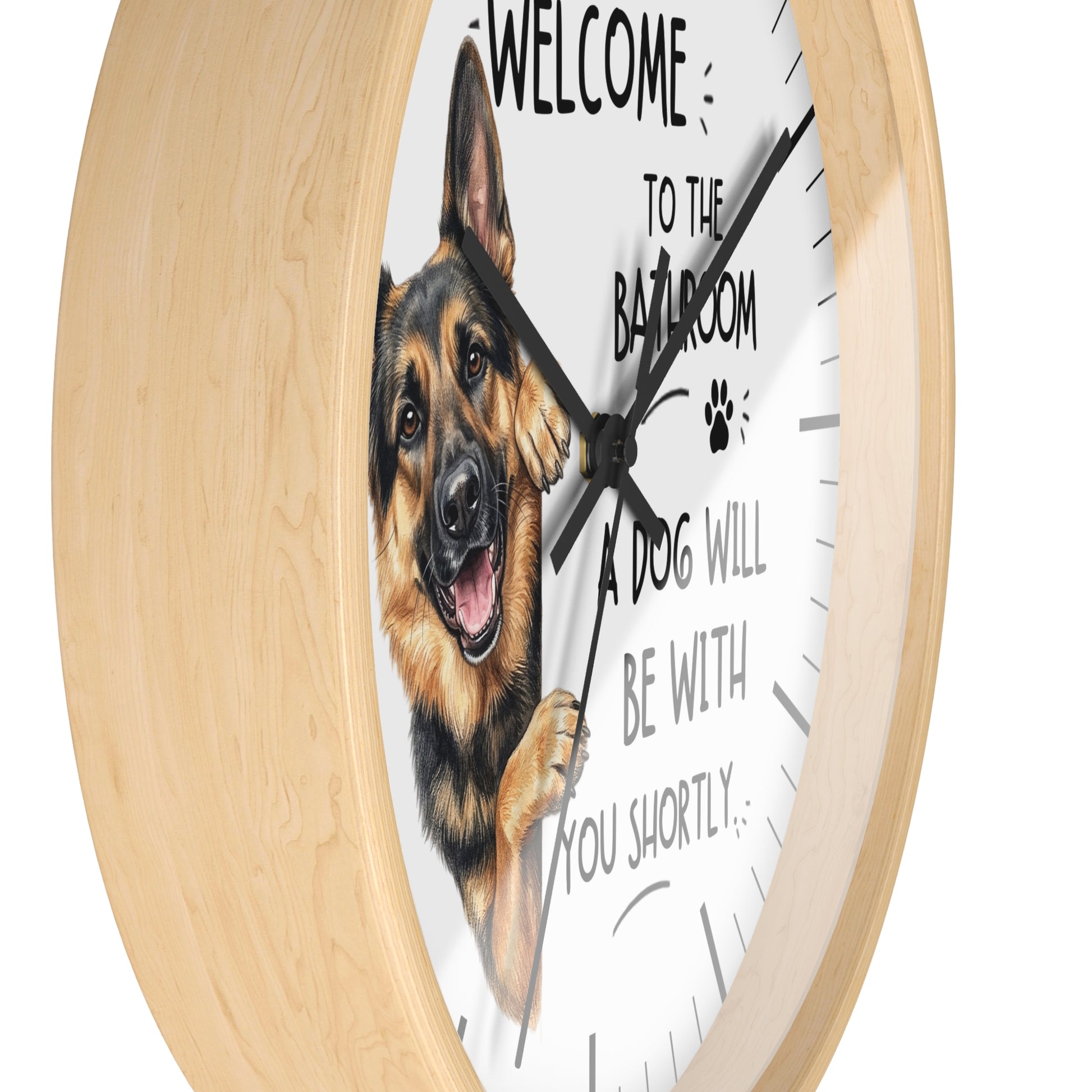 A round wall clock with a light natural wood frame and a white face featuring a German Shepherd illustration and the text 'WELCOME TO THE BATHROOM A DOG WILL BE WITH YOU SHORTLY.