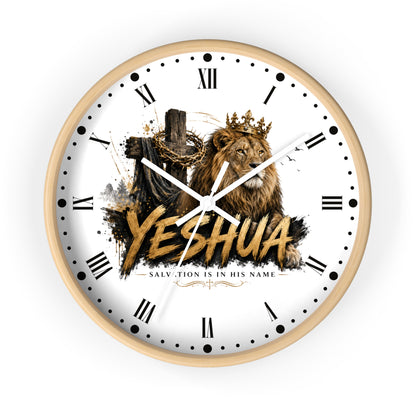 A round wall clock with a light wood frame and a white face featuring a graphic of a crowned lion, a cross with chains, and the word 'YESHUA' in large gold letters. The clock has black Roman numerals and white hands, shown against a plain white background.