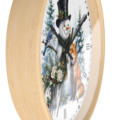 Round wall clock with a light natural wood frame and a white face featuring a winter illustration of a snowman in a top hat, a bluebird, a fox, evergreen trees, and flowers.