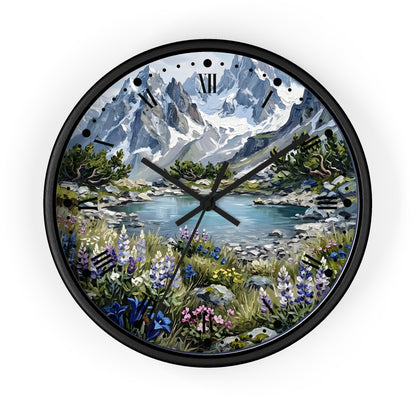 A round wall clock with a black frame and a scenic landscape print featuring snow-capped mountains, a lake, and wildflowers. The clock face has black Roman numerals and black hands, shown against a plain white background.