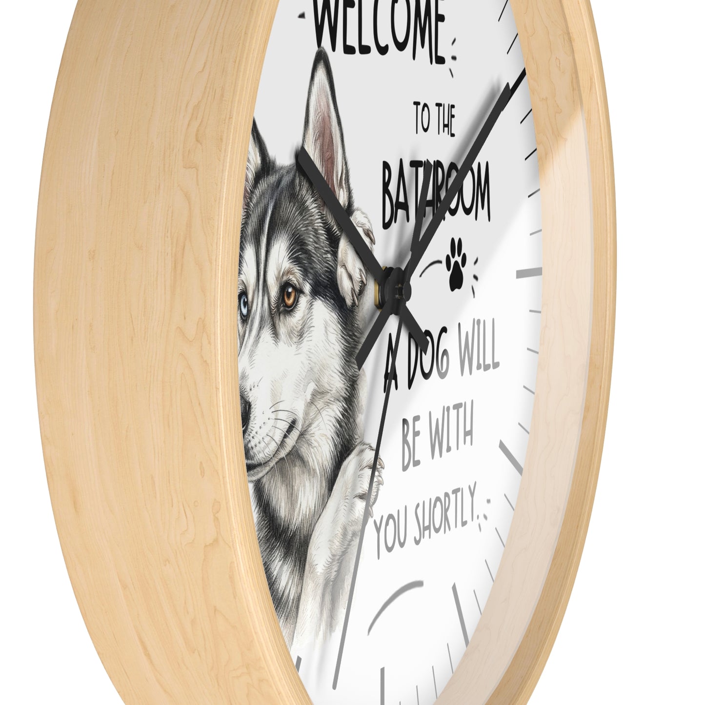 A round wall clock with a light natural wood frame and a white face featuring a husky illustration and the text 'WELCOME TO THE BATROOM A DOG WILL BE WITH YOU SHORTLY'.