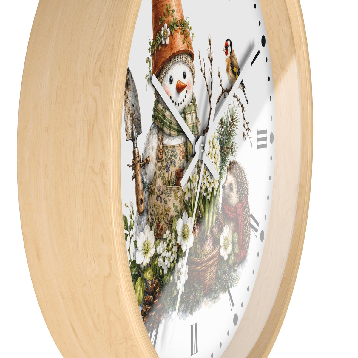 A round wall clock with a light natural wood frame and a white face featuring a whimsical winter garden illustration. The design includes a snowman wearing a gardening hat and apron, holding a trowel, with white flowers, evergreen branches, a bird, and a basket of produce.