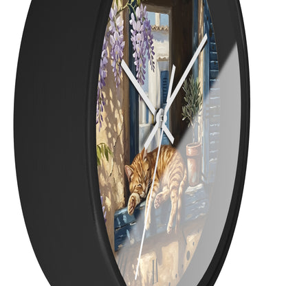 Round wall clock with a black frame and a printed illustration of an orange tabby cat sleeping on a windowsill, with purple wisteria and a sunlit balcony scene.
