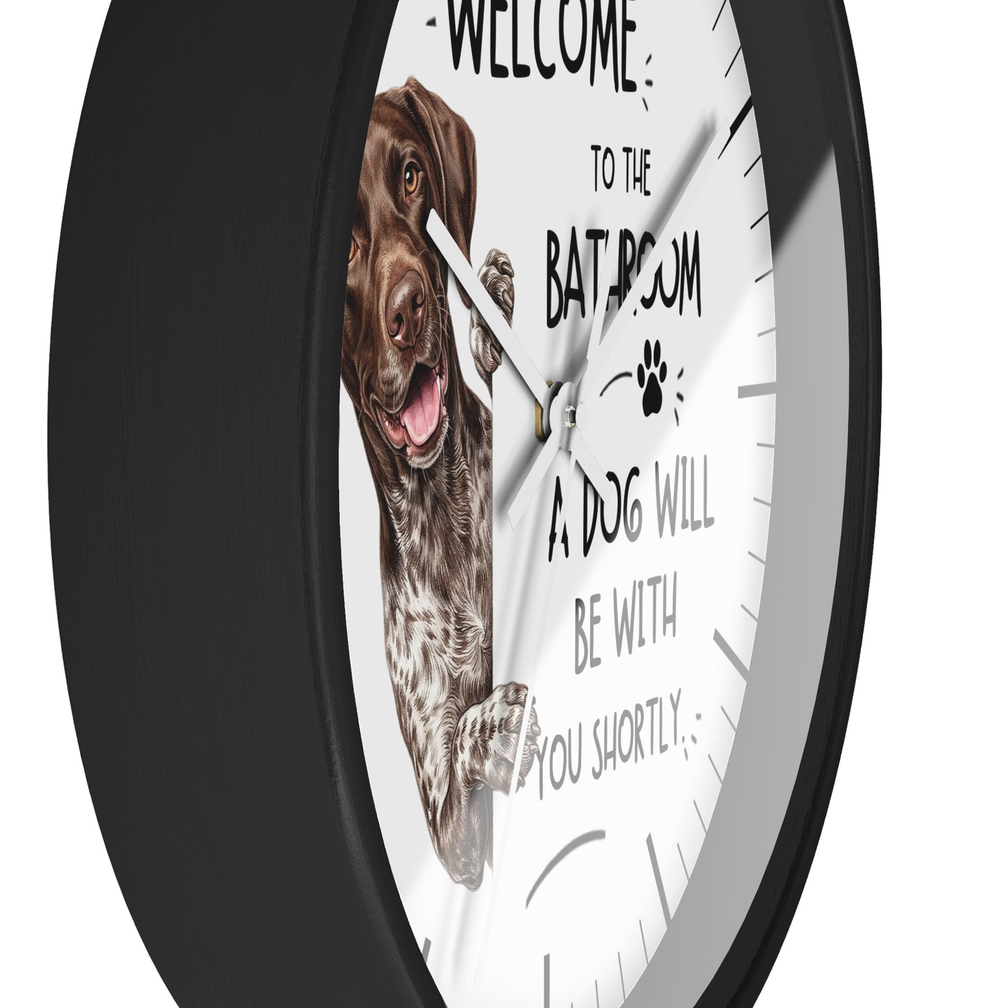 A round wall clock with a black frame and a white face featuring a brown dog illustration and the text 'WELCOME TO THE BATHROOM A DOG WILL BE WITH YOU SHORTLY'.