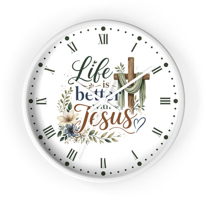 A round white wall clock with a Christian-themed graphic that reads 'Life is better with Jesus' in stylized script and serif fonts, decorated with a wooden cross draped in green cloth, floral elements, and black Roman numerals with dot hour markers.