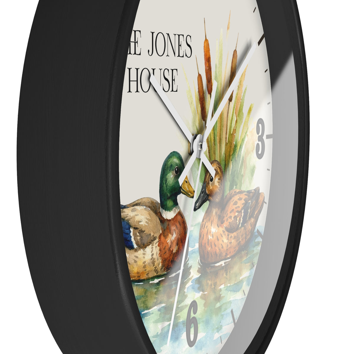 A round wall clock with a black frame and a printed duck scene on the face. The dial shows two ducks, cattails, partial numerals, and the text 'THE JONES HOUSE'.