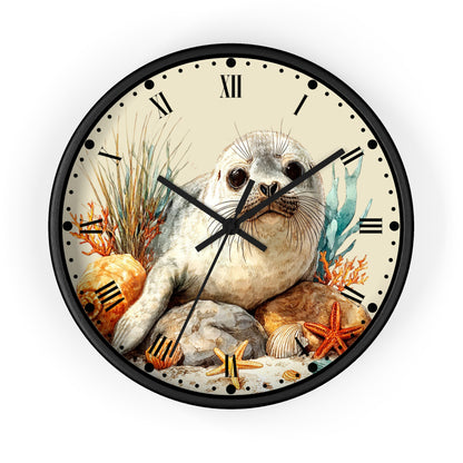 Round wall clock with a black frame and Roman numerals, featuring an illustrated seal sitting among rocks, starfish, coral, and seashells on the face, shown against a plain white background.