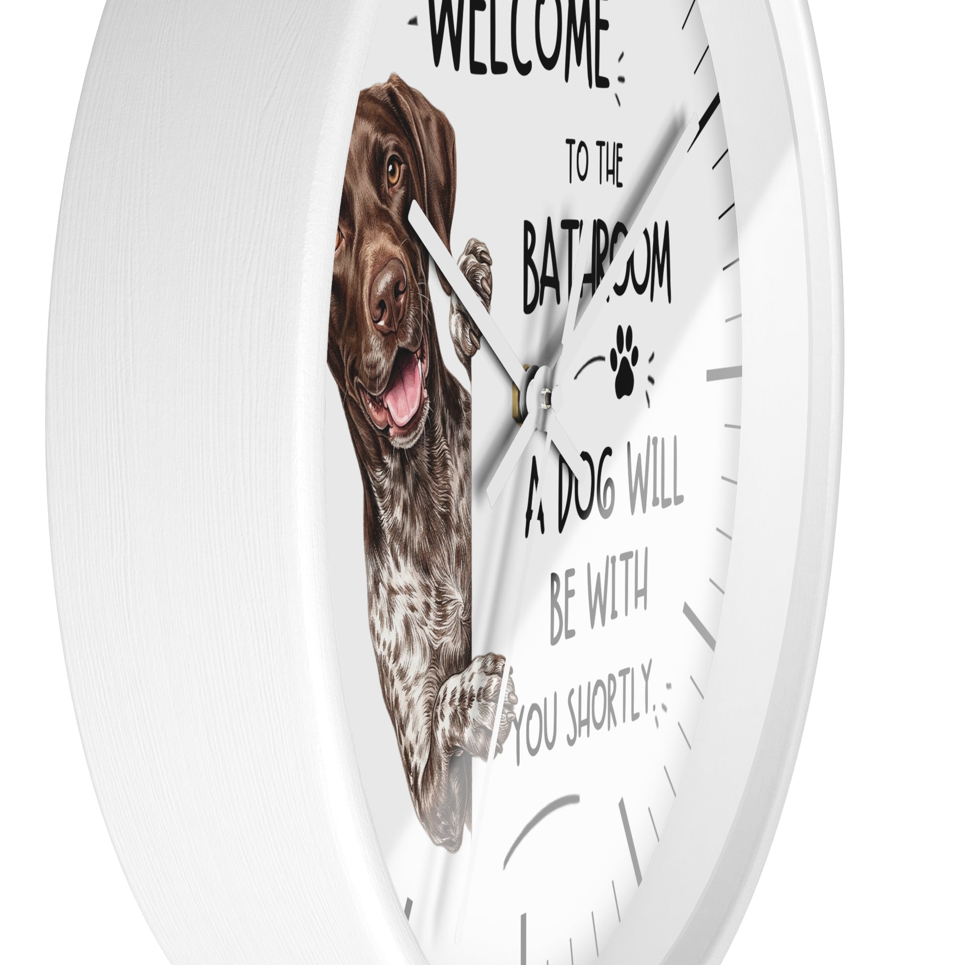 A white round wall clock with a printed design featuring a brown and white dog on the face, along with the text 'WELCOME TO THE BATHROOM A DOG WILL BE WITH YOU SHORTLY' and a paw print.