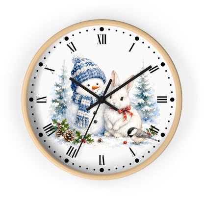A round wall clock with a light wood frame and a white face featuring a winter holiday illustration of a snowman in a blue knit hat and scarf next to a white rabbit with a red bow tie, with pine trees and a small bird. The clock uses black Roman numerals and black hands.