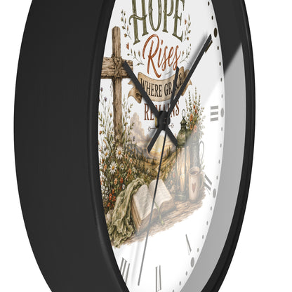 A close-up of a wall clock with a black frame and a white face featuring a rustic religious illustration with the words 'Hope Rises' and a cross.