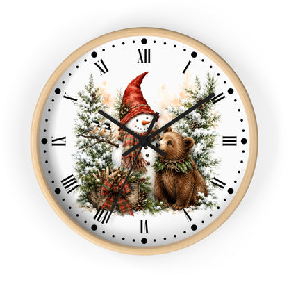 A round wall clock with a light wood frame and a white face featuring a winter holiday illustration of a snowman in a red hat among snowy trees, with a brown bear at the center. The clock is shown against a plain white background.