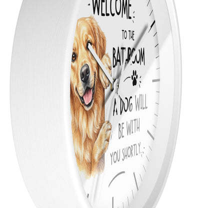 A white round wall clock with a printed face featuring a golden retriever illustration and the text 'WELCOME TO THE BATROOM A DOG WILL BE WITH YOU SHORTLY'.