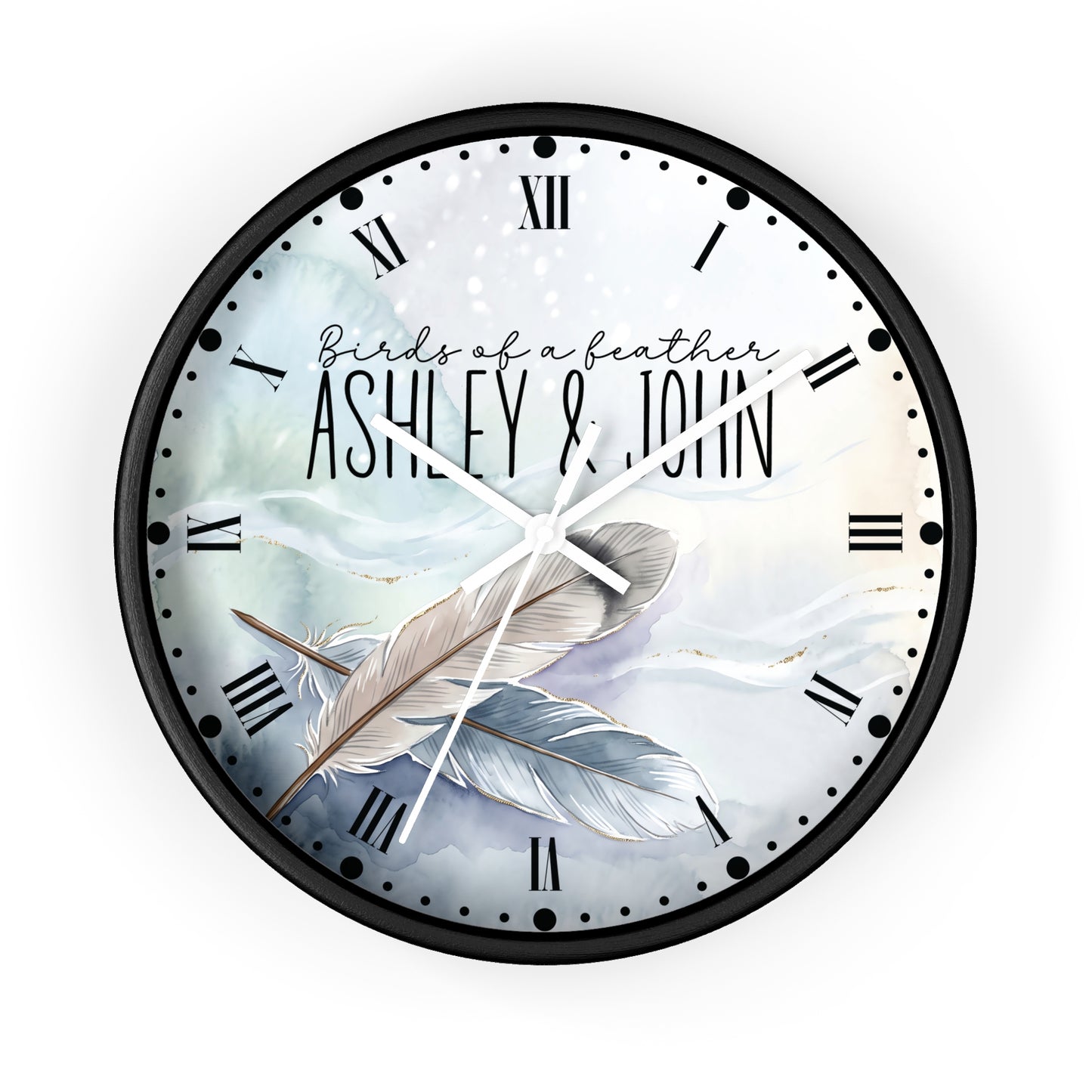A round wall clock with a black frame and a custom printed dial featuring the text 'Birds of a feather ASHLEY & JOHN' over an illustration of two feathers on a soft blue and white background.