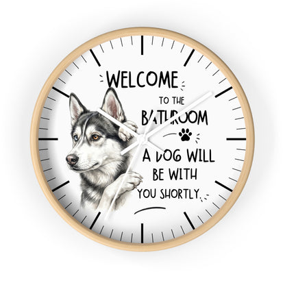 A round wall clock with a light wood frame and a white face, featuring a detailed illustration of a husky dog and the humorous text 'WELCOME TO THE BATHROOM A DOG WILL BE WITH YOU SHORTLY'.