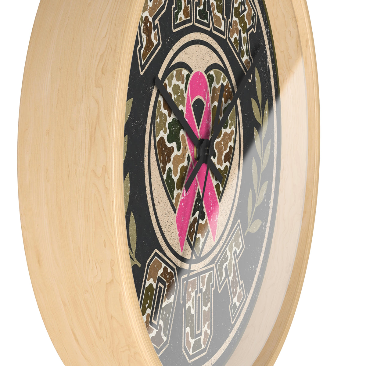 A close-up of a round wall clock with a light natural wood frame and a printed dial featuring a pink ribbon over a camouflage heart, set against a plain white background.