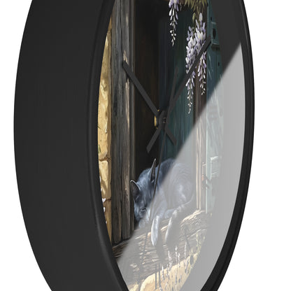 Round wall clock with a black frame and a printed illustration of a gray cat lying on a stone floor beside a dark wooden door and wisteria flowers, shown against a white background.