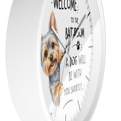 A white round wall clock with a printed illustration of a small dog and the text 'WELCOME TO THE BATHROOM A DOG WILL BE WITH YOU SHORTLY' on a clean white background.
