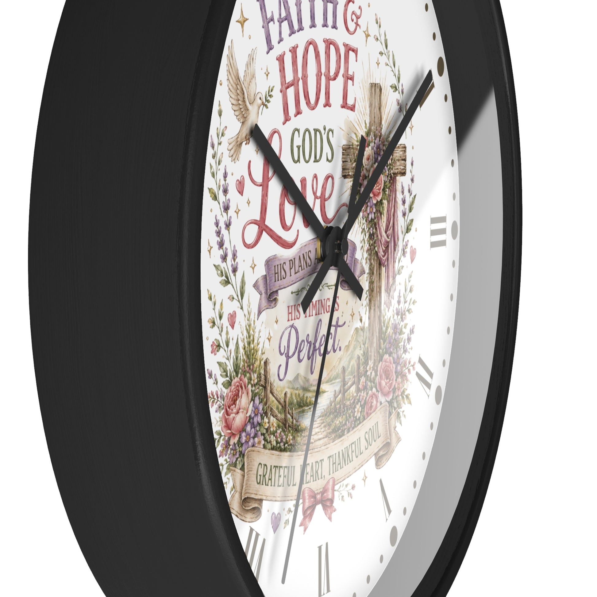 A close-up of a wall clock with a black frame and a white face featuring a Christian inspirational design with a cross, doves, floral elements, and religious text.