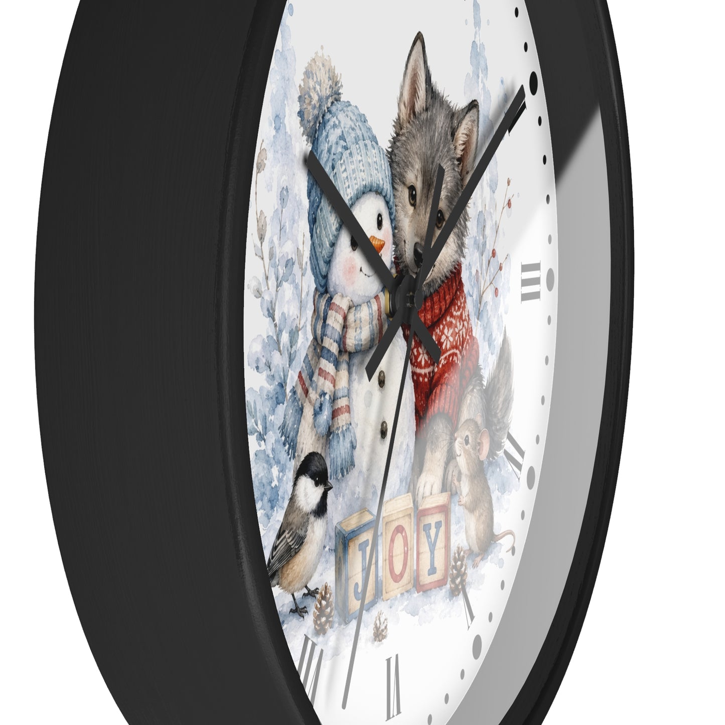 A round wall clock with a black frame and a whimsical winter illustration on the face. The artwork shows a penguin in a blue knit hat and scarf, a gray wolf wearing a red sweater, a small bird, and the word "JOY" in colorful blocks, all on a white background.