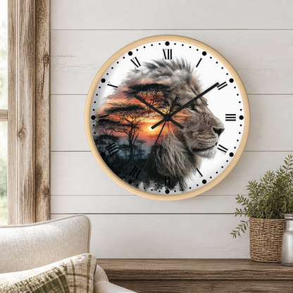 A round wall clock with a light wood frame hangs on a white shiplap wall above a wooden table. The clock face features a photographic lion profile layered over a savanna sunset scene with acacia trees.