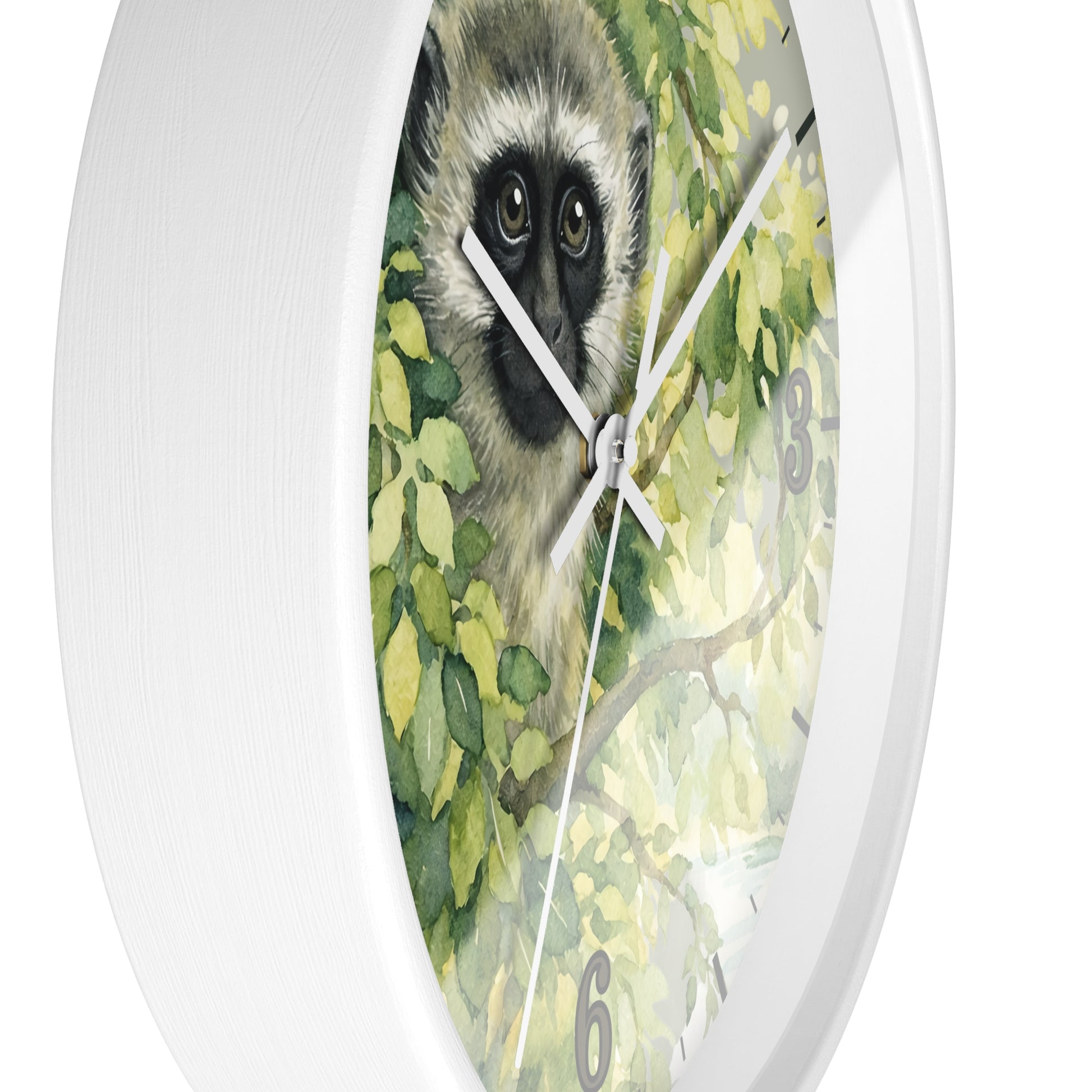 A round white wall clock with a printed face featuring a vervet monkey surrounded by green leaves, shown against a plain white background.