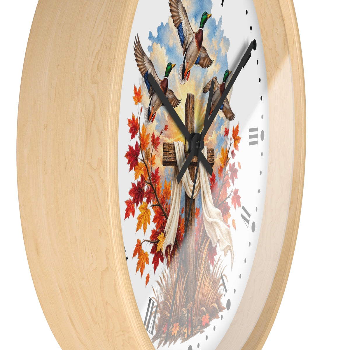 Round wall clock with a light natural wood frame and a white face featuring three mallards flying above autumn leaves, a wooden cross, and a white cloth, shown on a white background.