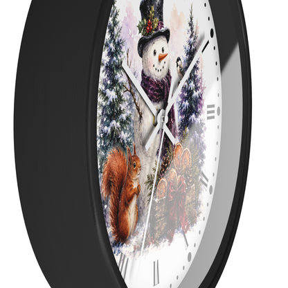 A round wall clock with a black frame and a white face featuring a winter illustration of a snowman, evergreen trees, a red squirrel, and a small bird, shown against a plain white background.