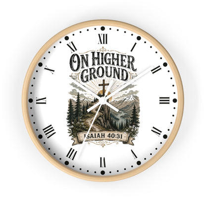 A round wall clock with a light wood frame and a white face featuring the text 'ON HIGHER GROUND' and 'ISAIAH 40:31' over a scenic mountain-and-trees illustration. The clock uses black Roman numerals and hands on a clean white background.
