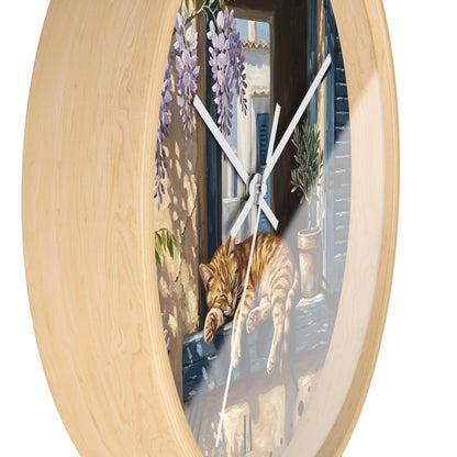 Round wall clock with a light natural wood frame and a printed illustration of an orange tabby cat sleeping on a windowsill, with purple wisteria and a blue-toned window background.