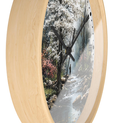 Round wall clock with a light natural wood frame and a printed scenic artwork of a forest stream, shown against a plain white background.