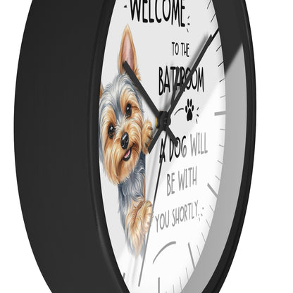 A round wall clock with a black frame and a white face featuring an illustration of a Yorkshire Terrier and the text 'WELCOME TO THE BATHROOM A DOG WILL BE WITH YOU SHORTLY'.