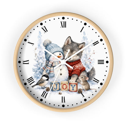 A round wall clock with a light wood frame and a white face featuring a winter illustration of a wolf, snowman, bird, mouse, and the word 'JOY' in wooden blocks. Roman numerals mark the hours, and the clock is shown against a plain white background.