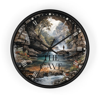 A round wall clock with a black frame and a scenic cave landscape print, featuring the text 'THE CAVE' over the center. The clock is shown against a plain white background.
