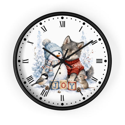 A round wall clock with a black frame and a white face featuring a winter illustration of a wolf, snowman, bird, and mouse around the word 'JOY' in wooden blocks, with Roman numerals as hour markers.