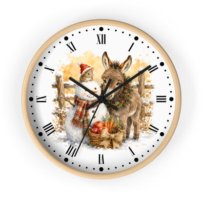 A round wall clock with a light wood frame and a white face featuring a festive winter illustration of a snowman and a donkey, with black Roman numerals and hands on a white background.
