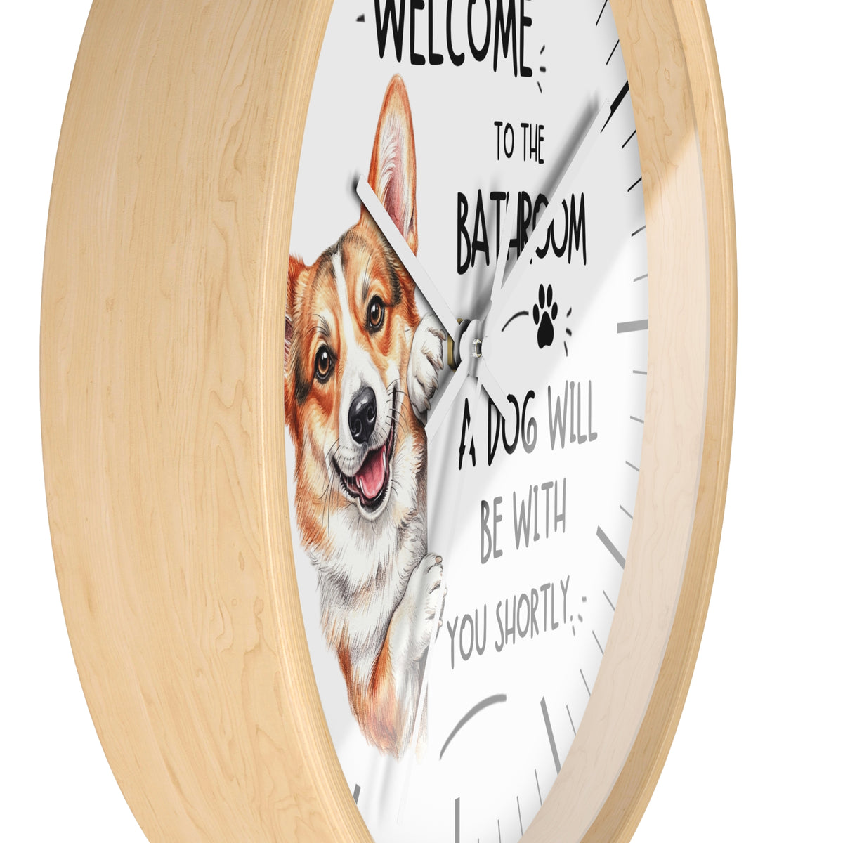 A round wall clock with a light natural wood frame and a white face. The clock face features a painted corgi illustration and the humorous text 'WELCOME TO THE BATROOM A DOG WILL BE WITH YOU SHORTLY'.
