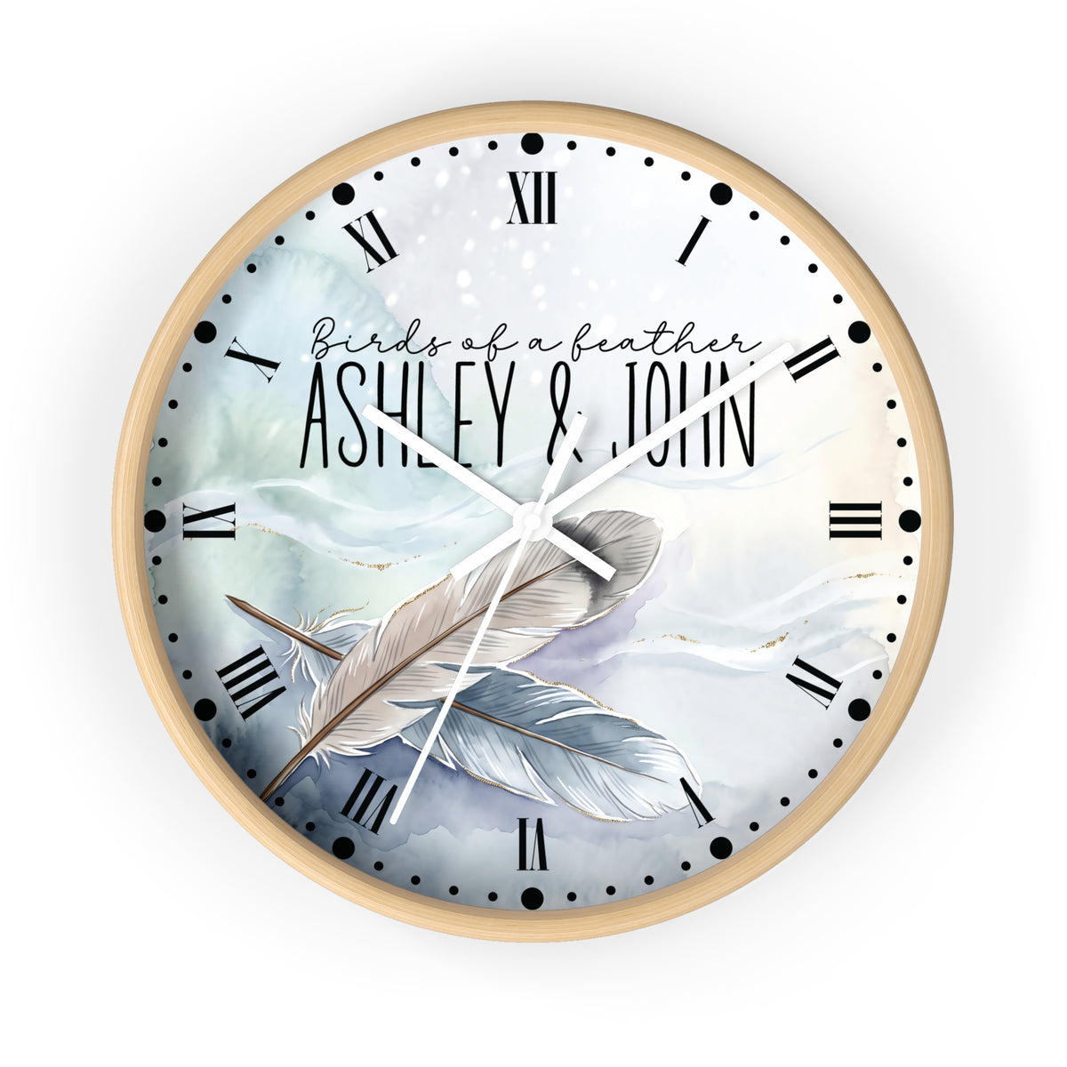 A round wall clock with a light wood frame and a custom printed dial featuring the text 'Birds of a feather ASHLEY & JOHN' over a watercolor illustration of two feathers in soft blue, white, and gray tones. The clock has black Roman numerals and white hands, shown against a plain white background.
